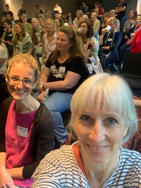 Selfie von Birgit Krüger mit Martina Leeb und weiteren Teilnehmerinnen beim TCS-Barcamp 2025 in Dtuttgart 2025, Blick ins gut gefüllte Publikum.