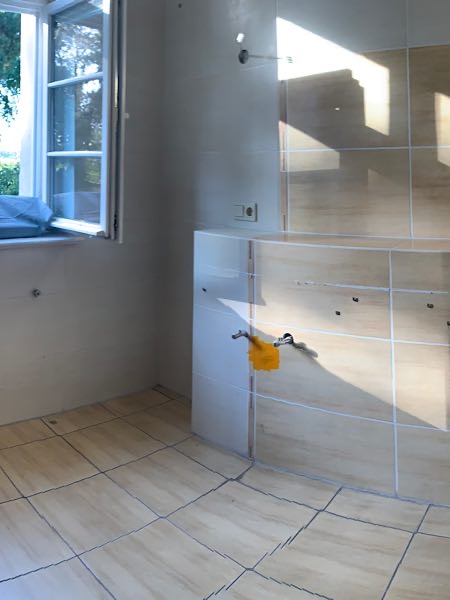 Leeres Badezimmer mit Fliesenboden, offenem Fenster und vorbereiteten Anschlüssen für ein Waschbecken.