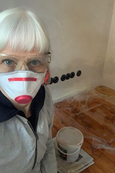 Frau mit weißen Haaren, mit Atemschutzmaske und Schutzbrille auf Holzboden