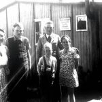 Schwarz-weißes Bild aus den späten 1940er Jahren zeigt eine Familie mit drei Kindern vor einer Baracke