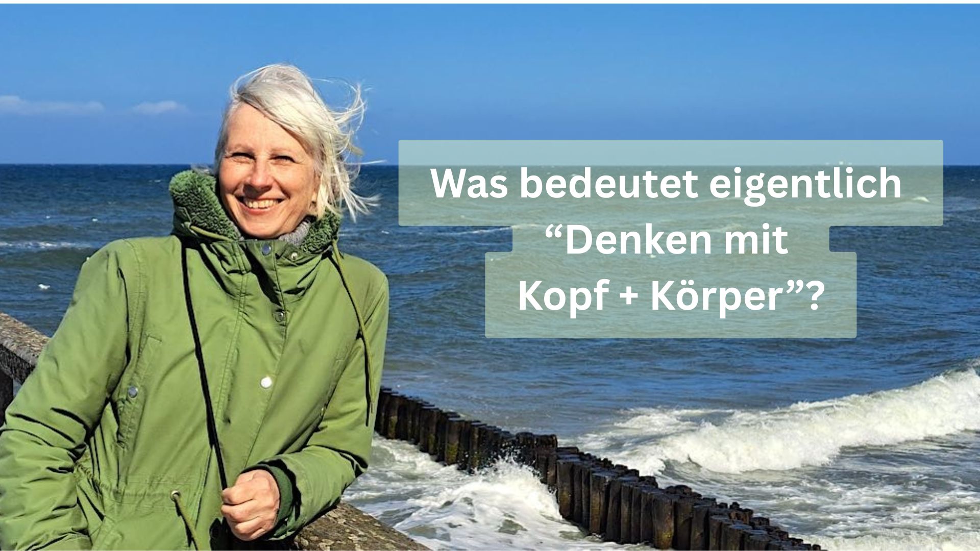 Birgit Krüger in grüner Jacke lächelt am windigen Meer; Text im Bild: „Was bedeutet eigentlich Denken mit Kopf + Körper?“