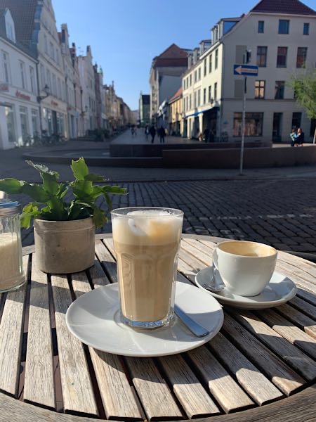 Zwei Kaffees auf einem Holztisch in der Sonne – Blick in die Fußgängerzone von Wismar. Ein Moment der Pause für Focusing-Coach Birgit Krüger