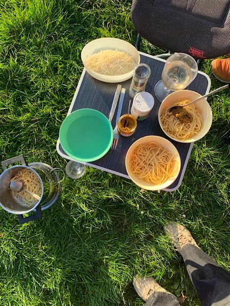 Abendessen auf kleinem Campingtisch: Spaghetti, Parmesan, Gewürze und zwei Weingläser – ein typisches Camper-Essen, festgehalten von einem Focusing-Coach auf Reisen.